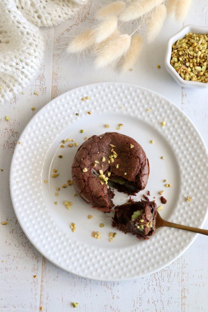 Moelleux au chocolat avec un coeur coulant à la pistache sur une assiette blanche. Eclats de pistache.
